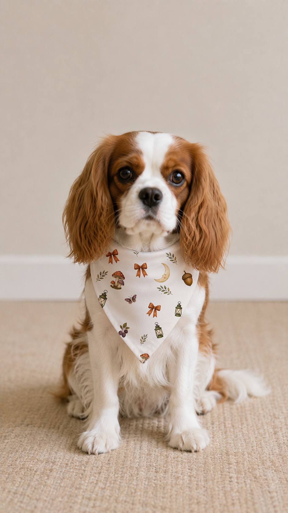 A Cavalier King Charles Spaniel dog wearing a cream bandana with a small yellow floral pattern, sitting on a beige carpeted floor against a neutral beige wall.