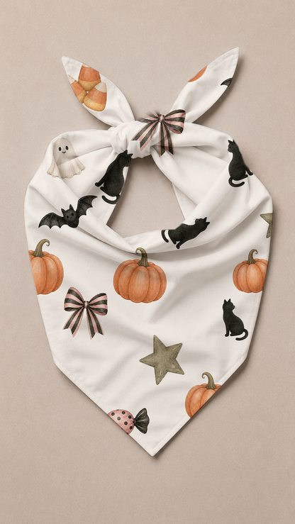 A white pet bandana with a knotted top, featuring a Halloween print of orange pumpkins, black cats, brown bows, a gray star, and a small ladybug, displayed flat against a neutral beige background.