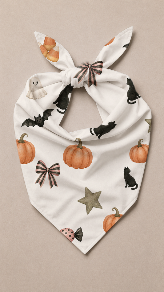A white pet bandana with a knotted top, featuring a Halloween print of orange pumpkins, black cats, brown bows, a gray star, and a small ladybug, displayed flat against a neutral beige background.