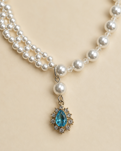 Close-up of blue teardrop pendant on pearl-style pet necklace