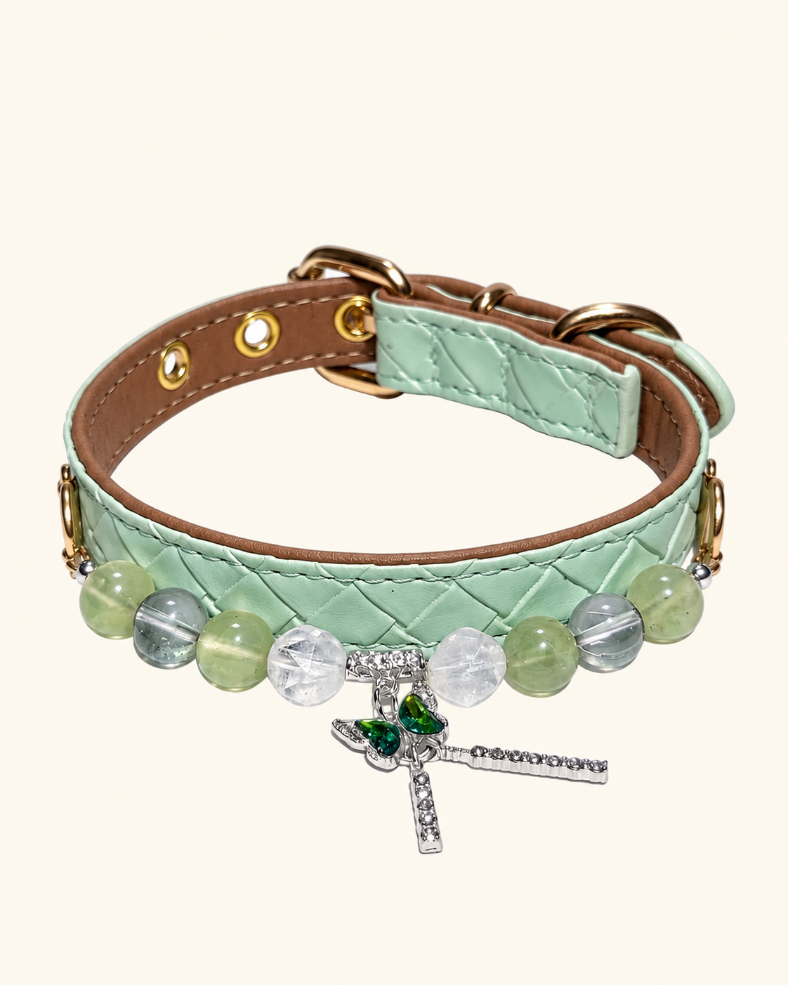 A quilted mint green collar with a brown leather interior, decorated with clear and light green faceted beads, gold-tone hardware, and a dangling dragonfly charm embellished with green and clear crystals.