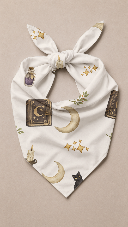 A white tie-front bandana or scarf featuring a whimsical occult-themed print with gold crescent moons, stars, a purple potion bottle, a black cat, and a brown journal, displayed flat on a neutral beige background.