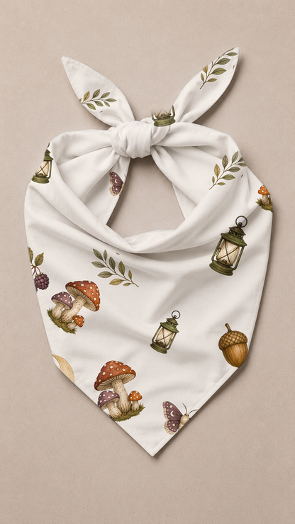 A white triangular bandana with a knotted bow, featuring an all-over print of mushrooms, lanterns, acorns, and leaves on a neutral beige background.
