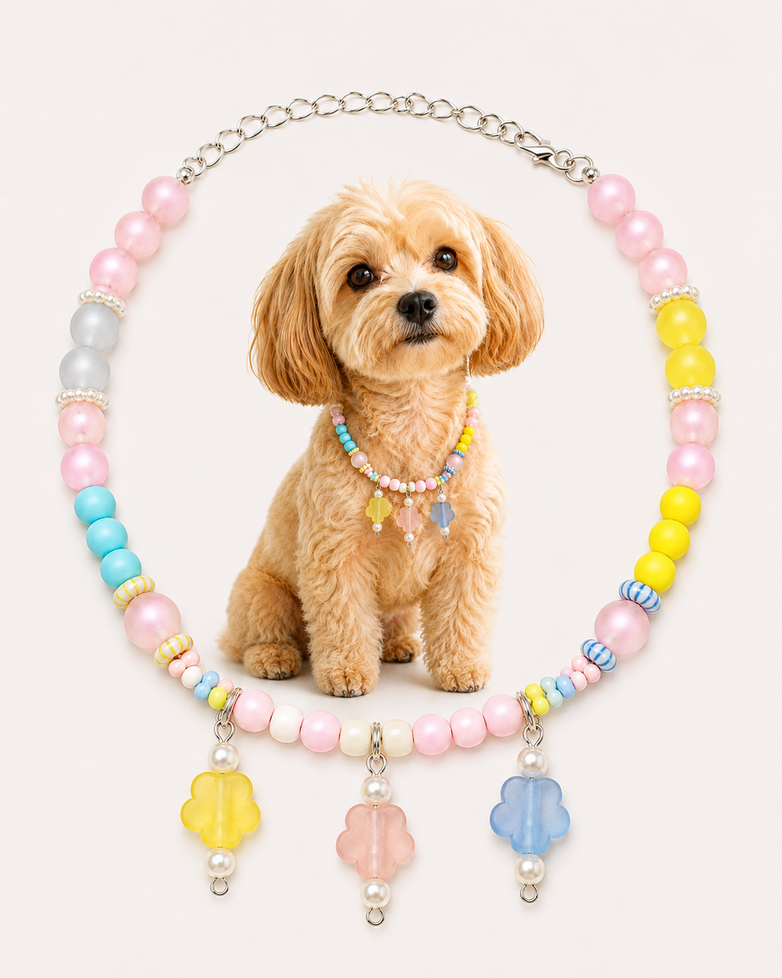 A small fluffy tan dog sits centered against a light warm background, wearing a pastel beaded collar necklace with pink, yellow, blue, and white beads plus flower-shaped charms. The necklace is arranged in an oval around the dog, and the dog itself is the main visible subject, so this is classified as Lifestyle rather than Product/Packaging.