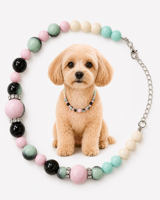A beaded dog collar necklace with pastel pink, mint green, light blue, cream, and black beads, shown on a white background with a small tan dog wearing a smaller version of the necklace.