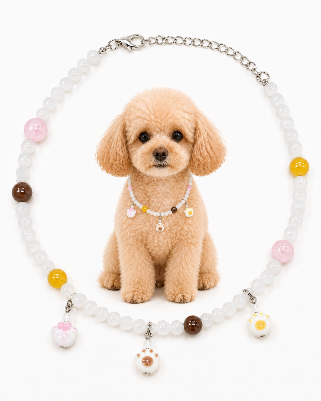 A small tan poodle sits centered in front of a beaded pet collar necklace on a white background. The necklace has translucent white beads, a silver chain, and colorful round beads and charms in pink, yellow, brown, and white with a paw-print detail.