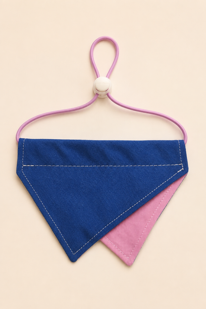 A fabric pet bandana in blue and pink with white stitching, attached to a pink elastic loop with a white plastic slider, shown on a solid beige background.