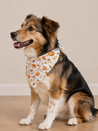 A tricolor dog sitting on a light wood floor against a beige wall, wearing a white bandana with a pumpkin and autumn leaf pattern.