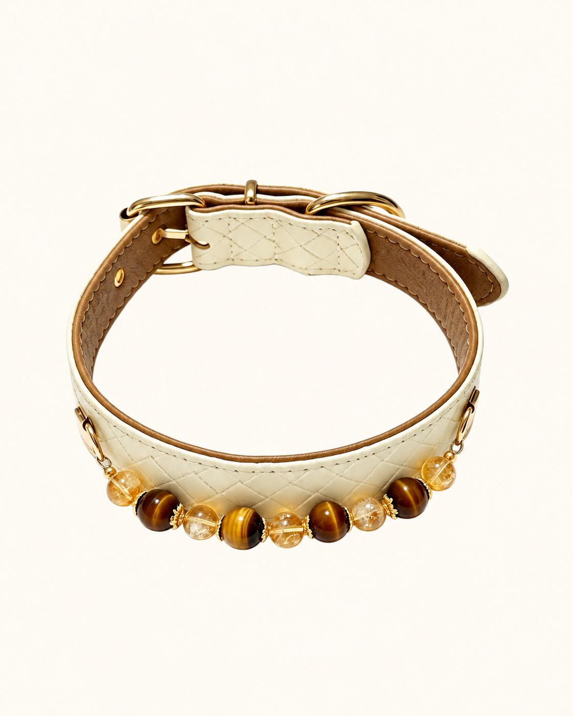A cream-colored quilted faux leather collar with gold-tone hardware, featuring a row of decorative beads including tiger's eye and clear crystal accents, displayed on a clean off-white background.