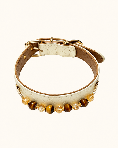 A cream-colored quilted faux leather collar with gold-tone hardware, featuring a row of decorative beads including tiger's eye and clear crystal accents, displayed on a clean off-white background.