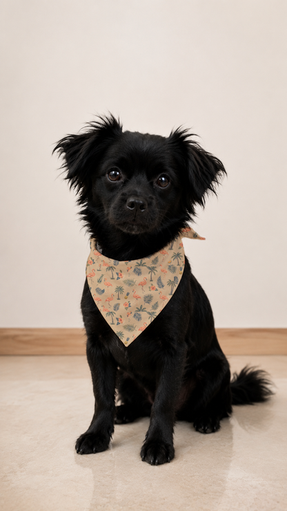 A small black dog wearing a beige bandana with a delicate floral pattern, sitting on a light beige floor against a neutral cream wall.