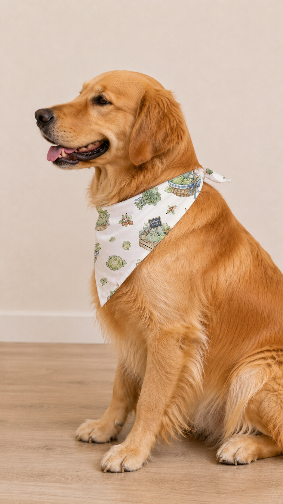 A golden retriever dog sitting on a light wood floor against a beige wall, wearing a white triangular bandana with a green and blue sea creature pattern.