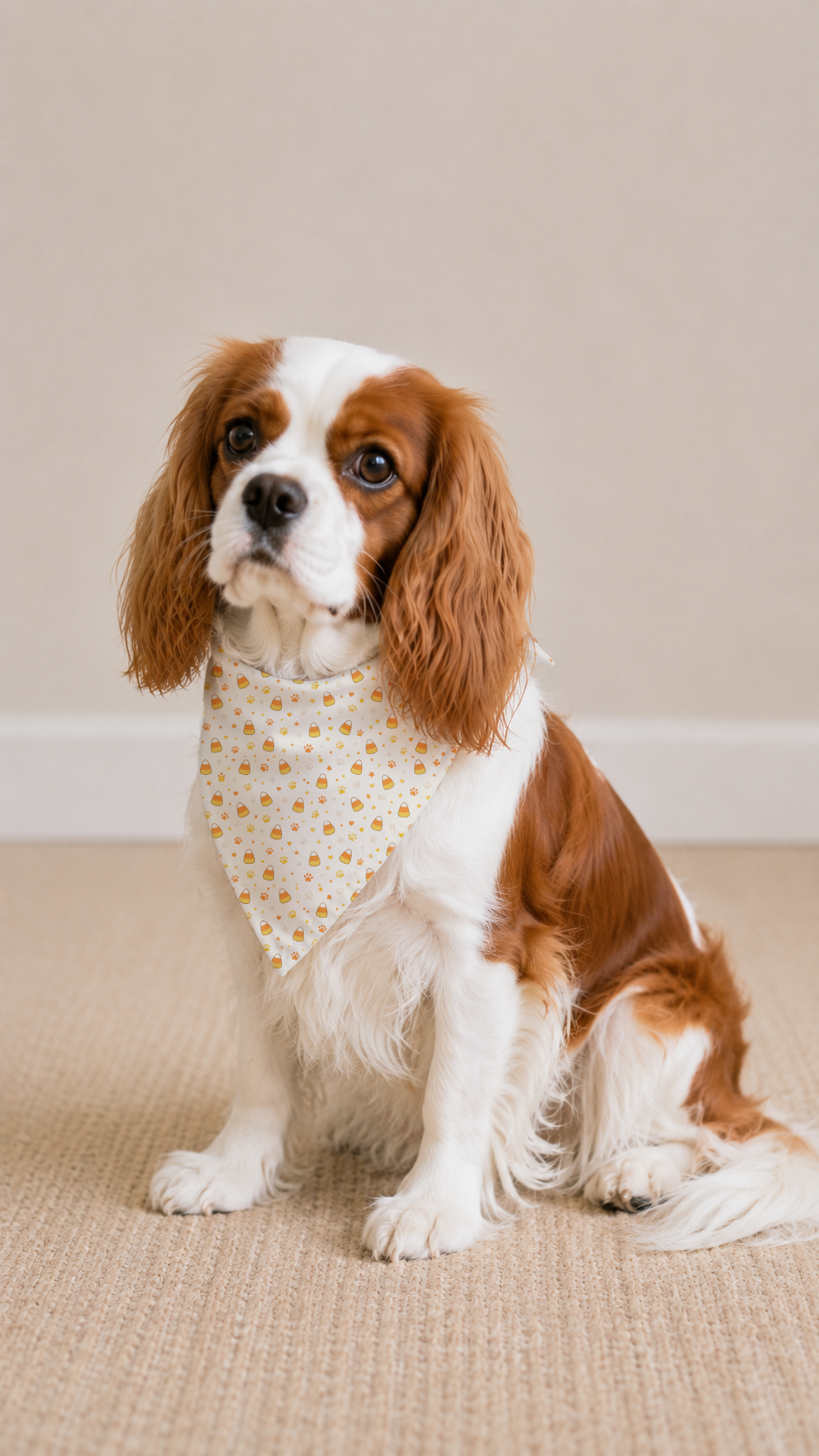 A small brown and white dog wearing a cream bandana with small yellow floral prints, sitting on a beige textured rug against a plain beige wall.