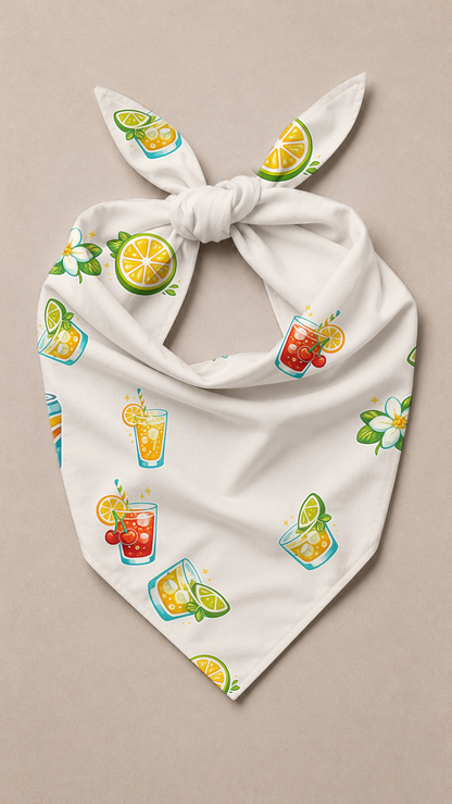 A white triangular bandana or pet bandana with a knotted top, featuring a colorful print of cocktail glasses, limes, and citrus slices, displayed flat on a neutral beige background.