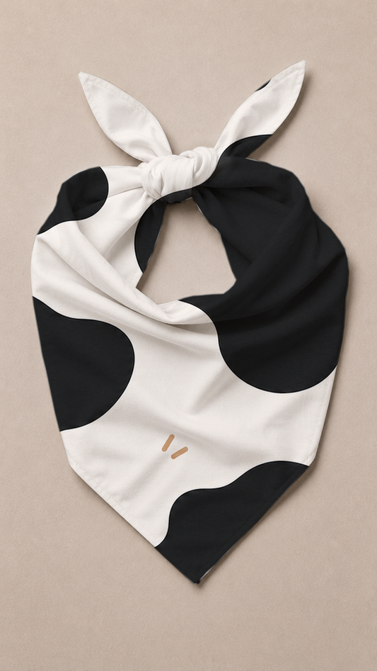A black and white cow-print neck scarf tied in a knot, displayed flat on a neutral beige background.