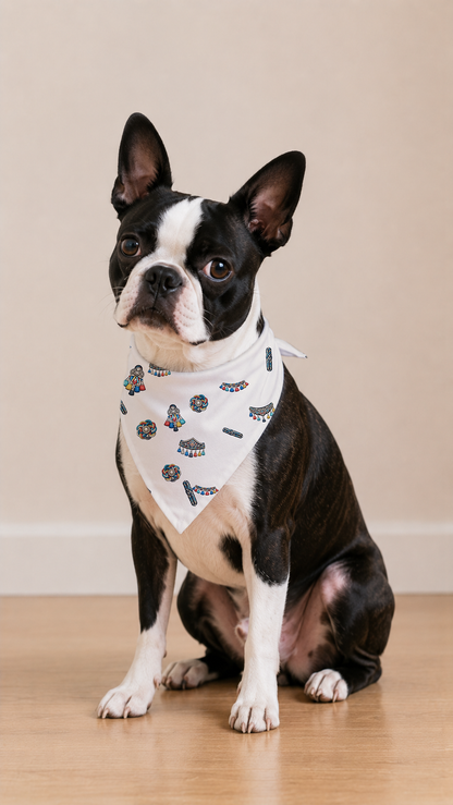 A Boston Terrier dog wearing a white bandana with a black and blue butterfly pattern, sitting on a light wood floor against a beige wall.