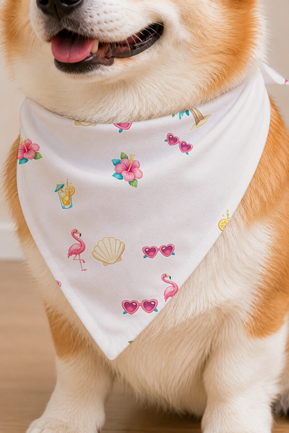 A close-up of a Shiba Inu dog wearing a white pet bandana printed with pink flamingos, pink flamingo sunglasses, pink hibiscus flowers, and seashell motifs.