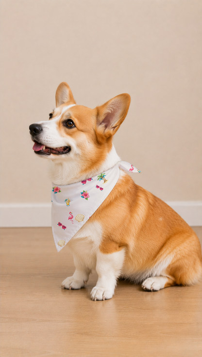 A corgi dog wearing a white bandana with a colorful flamingo and floral print, sitting on a light wood floor against a beige wall.