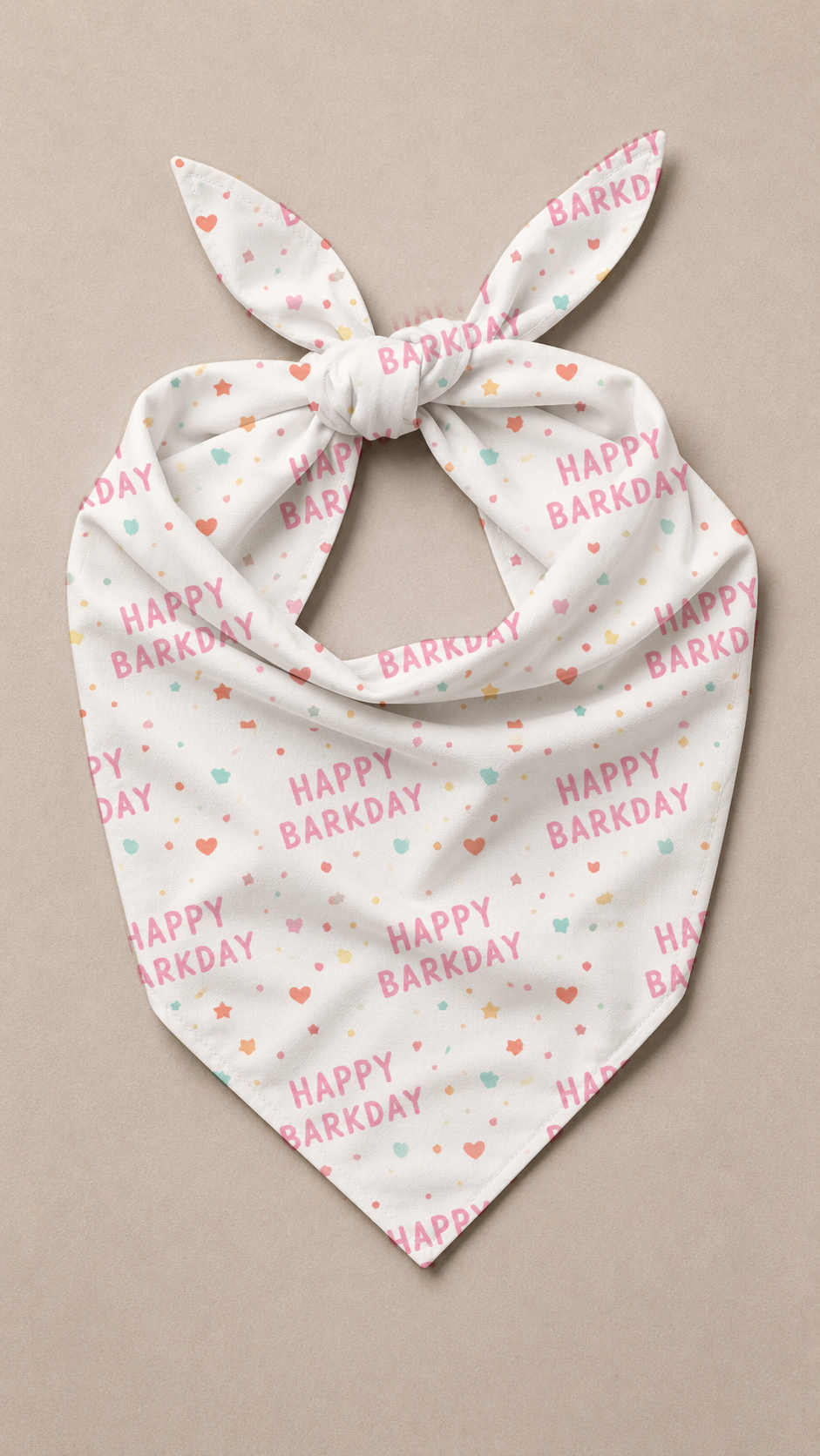 A white triangular pet bandana with a tie knot, featuring a repeating pattern of 'HAPPY BARKDAY' text in pink and small hearts in pink, orange, and mint green, displayed on a neutral beige background.
