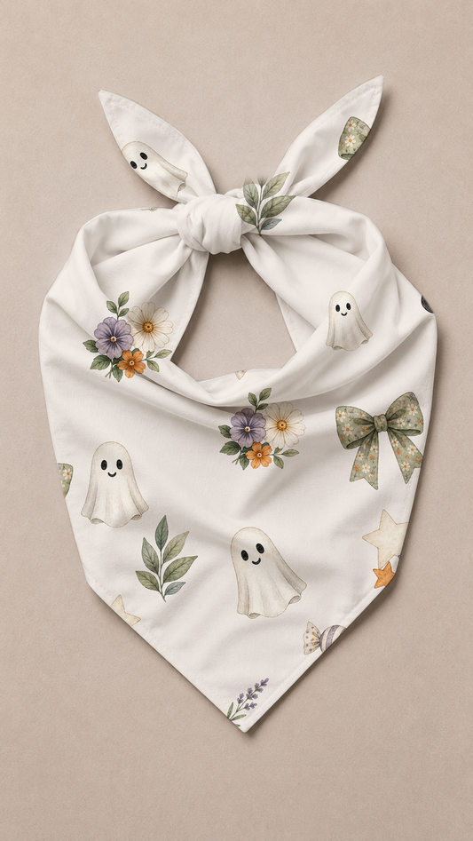 A white tie-on dog bandana featuring a cute ghost and floral pattern, displayed flat against a neutral beige background.