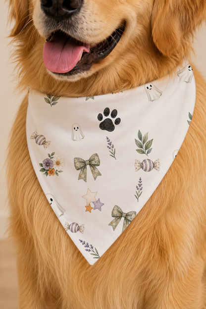 A golden retriever dog wearing a white triangular bandana with a cute ghost, paw print, bow, and floral pattern.