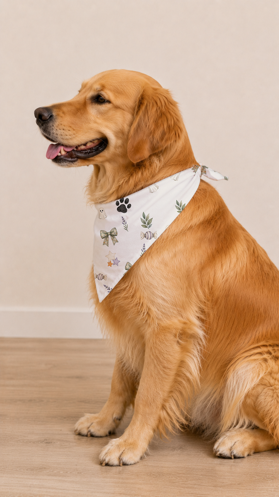 A golden retriever dog sitting on a light wood floor against a beige wall, wearing a white bandana with a green leaf pattern and a small black paw print.