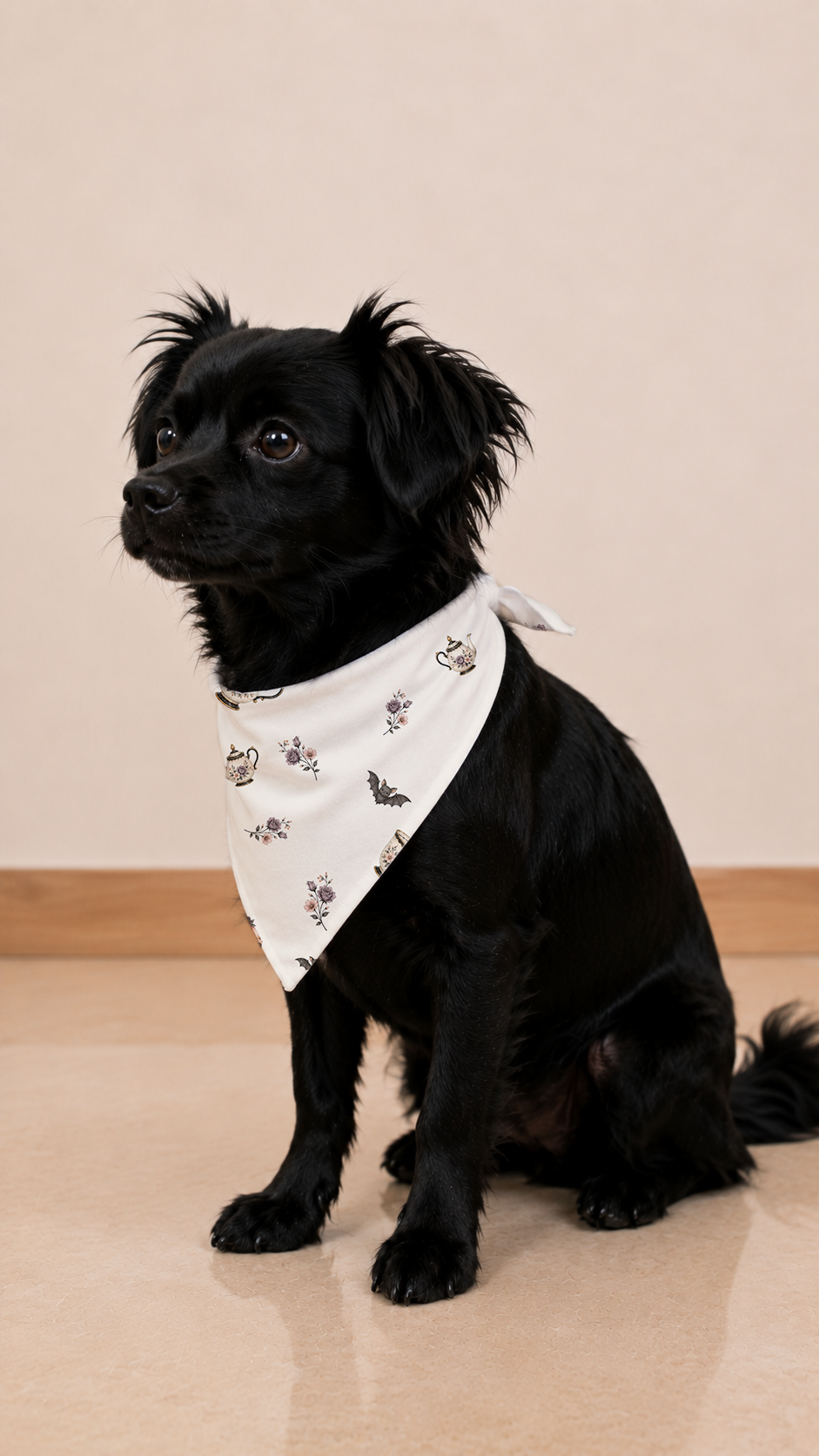 A small black dog wearing a white bandana with a small printed pattern, sitting on a beige tiled floor against a beige wall.