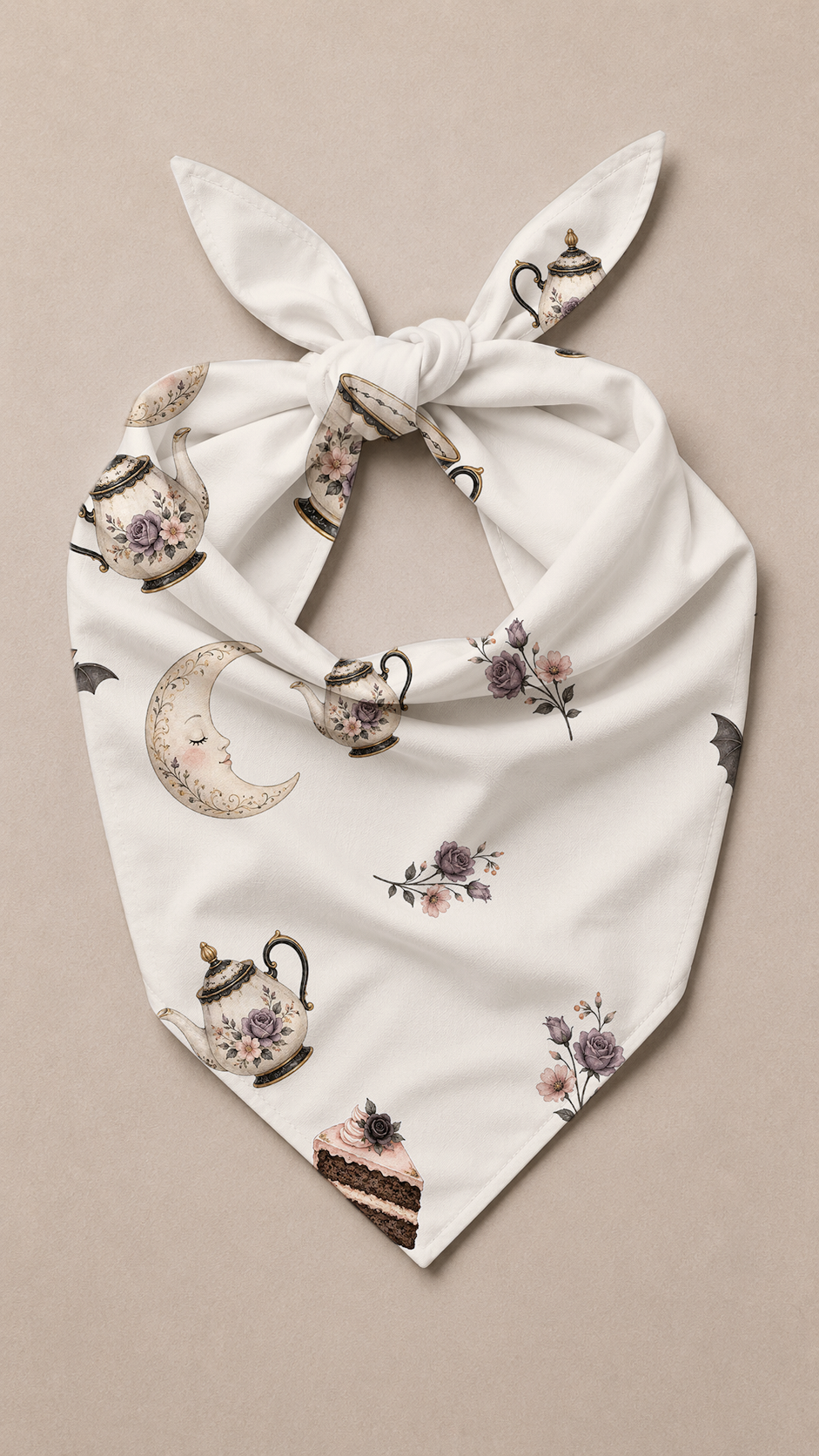 A white dog bandana with a knotted top, featuring a whimsical print of teapots, a crescent moon, and purple flowers, laid flat on a neutral beige background.