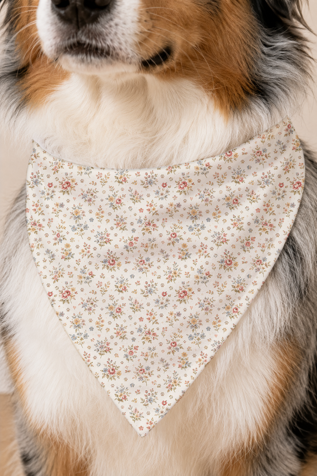 A close-up of a dog wearing a triangular bandana bib with a delicate multicolor floral pattern on a cream background.
