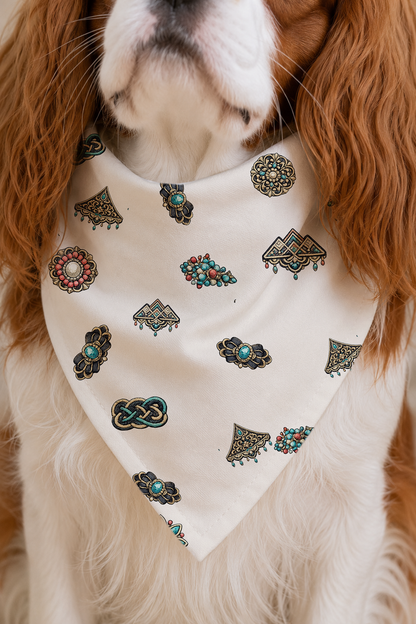 A close-up of a dog wearing a cream-colored bandana with colorful embroidered patterns, including turquoise and black details.