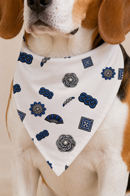 A close-up of a beagle dog wearing a white bandana-style pet collar printed with blue and gray decorative motifs, including flowers, knots, and geometric patterns.
