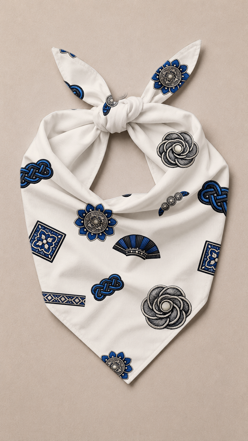 A white tie-front bandana or scarf featuring an all-over print of blue and gray decorative motifs, including flowers, geometric patterns, and fan shapes, laid flat on a light beige background.