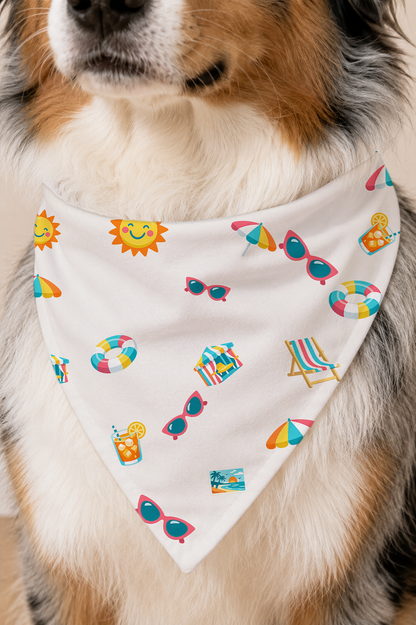 A close-up of a dog wearing a white triangular bandana with a colorful summer-themed print of sunglasses, beach umbrellas, a sun, a beach chair, and pool floats.