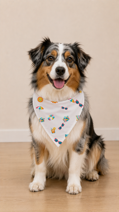 A tricolor Australian Shepherd dog sits on a light wood floor wearing a white triangular bandana with a colorful beach-themed pattern.