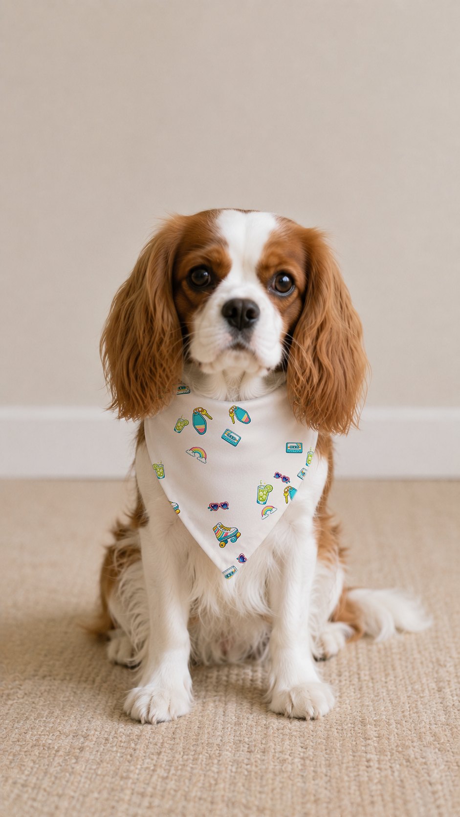A Cavalier King Charles Spaniel dog wearing a cream bandana with a small yellow floral pattern, sitting on a beige carpeted floor against a neutral beige wall.