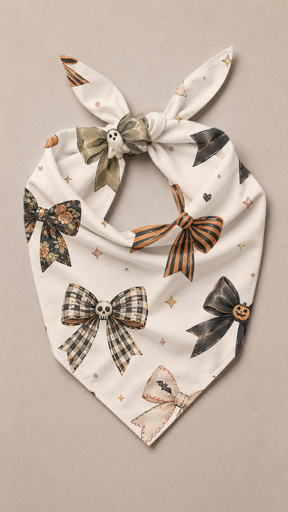 A white tie-front bandana or scarf featuring a Halloween-themed print of various bows, skulls, bats, and stars in black, orange, and brown, styled flat on a neutral beige background.