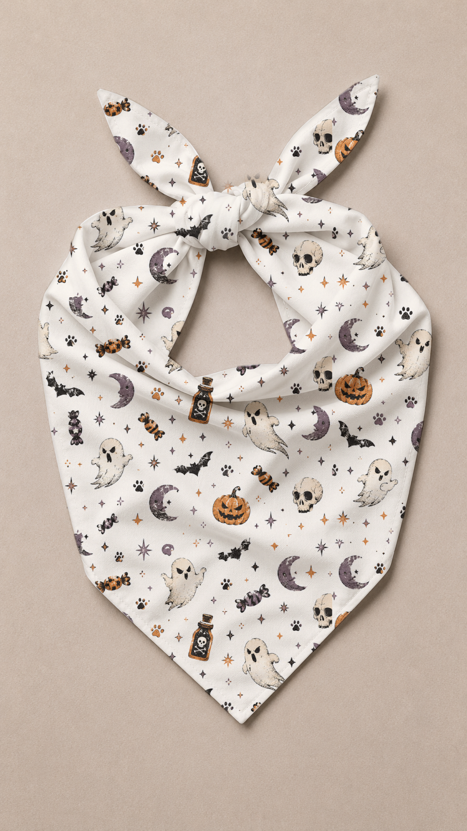 A white pet bandana with a knotted top and pointed bottom, featuring a repeating Halloween print of ghosts, pumpkins, bats, skulls, and moons, displayed flat against a neutral beige background.
