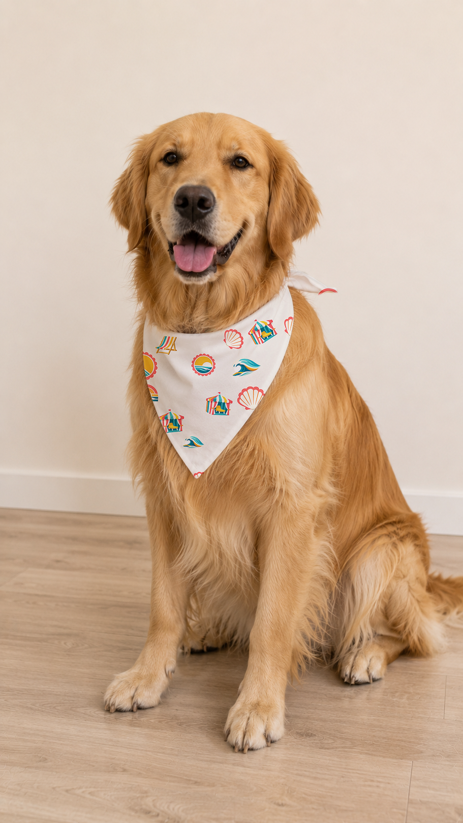 A golden retriever dog sitting on a light wood floor against a beige wall, wearing a white bandana with a colorful teddy bear pattern.